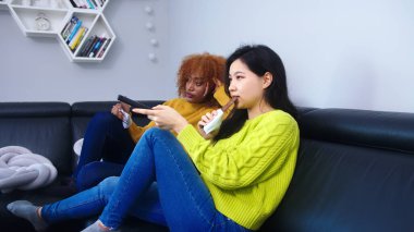 Televizyon izleyen ve çikolata yiyen iki lezbiyen kadın.