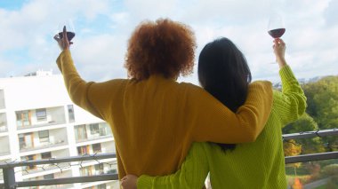 İki ırklar arası kız arkadaş balkonda şarap içiyor. . 