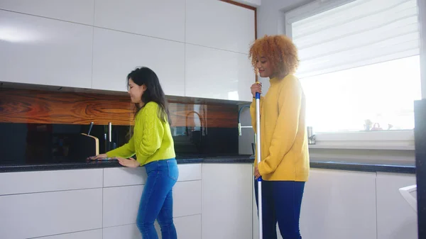 Melhores amigos companheiros de quarto se divertindo ao limpar a cozinha. Cantando e dançando com esfregona — Fotografia de Stock