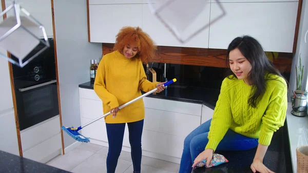 Duas jovens mulheres se divertindo enquanto fazem limpeza em casa. Amizade ou relacionamento multirracial — Fotografia de Stock