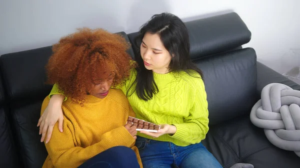 Genç Asyalı kadın üzgün Amerikalı Amerikalı siyahi arkadaşına çikolata ikram ediyor. Zor zamanlarda destek — Stok fotoğraf