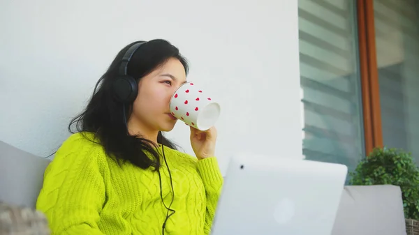 Joven mujer asiática con auriculares beber taza de té y navegar por las redes sociales. — Foto de Stock