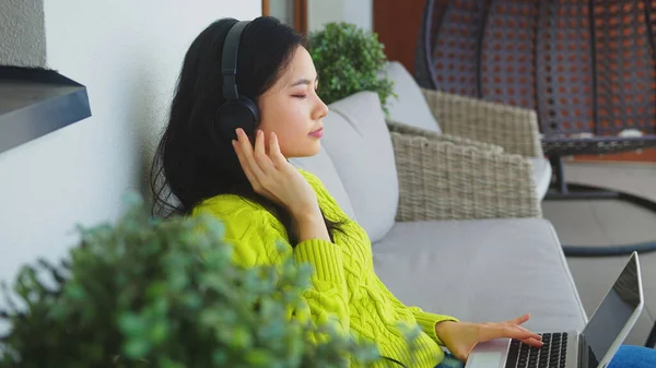 Joven mujer asiática escuchando la música de la computadora portátil usando auriculares — Foto de Stock