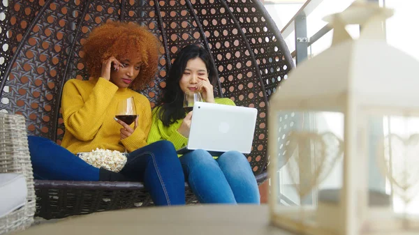 Duas mulheres, quartos multirraciais assistindo filme no laptop com vinho tinto e pipocas — Fotografia de Stock