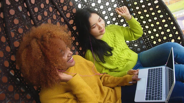 İki genç kadın dedikodu yapıyor ve sosyal ağlara takılıyor. Çok ırklı dostluk — Stok fotoğraf