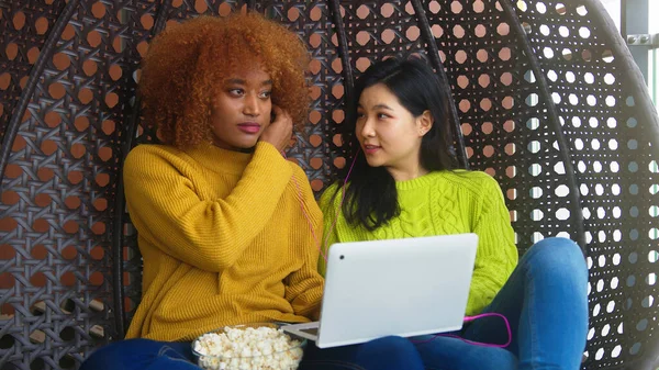 İki genç kadın kulaklıkları paylaşıyor ve laptoptan müzik dinliyor. Çok ırklı dostluk — Stok fotoğraf