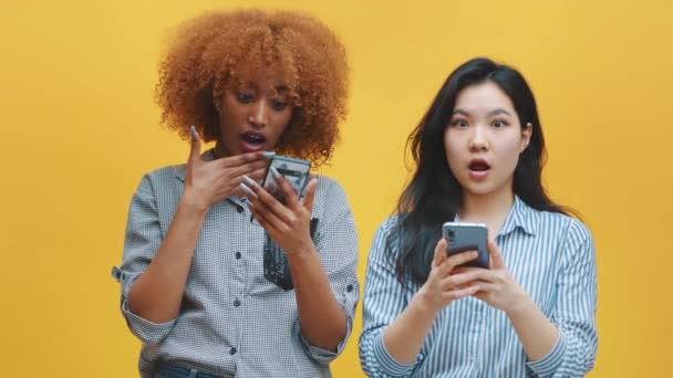 Jóvenes mujeres negras y asiáticas mirando las redes sociales post con la cara sorprendida — Vídeos de Stock