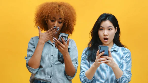 Две молодые женщины, проверяющие социальные сети и показывающие свое удивление со странным выражением лица — стоковое фото