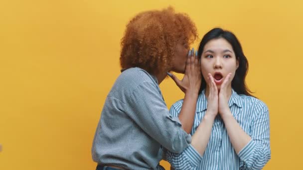 Jonge Afro-Amerikaanse zwarte vrouw die fluistert tegen haar Aziatische vriend die een shock uitte. Gossip meisjes en geheimen — Stockvideo