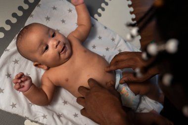 İlgilenen genç siyah baba yeni doğmuş bebeğinin karnını gıdıklıyor. Babalık ve çok ırklı aile