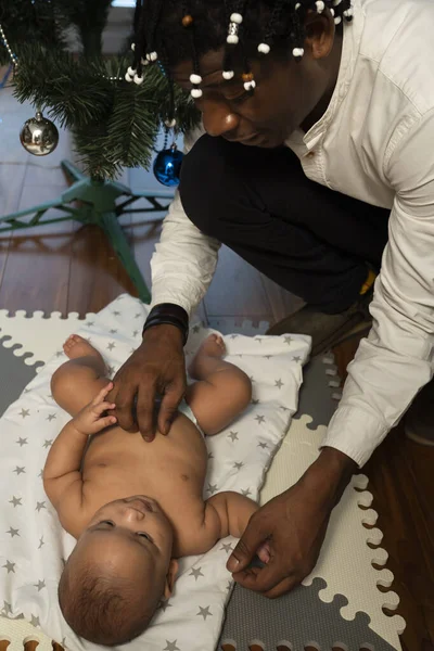 Bebê primeiro Natal. Jovem pai negro brincando com seu bebê mulato na frente da árvore de Natal — Fotografia de Stock