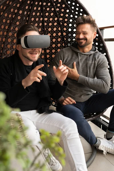 Виртуальный мир. Веселая гей-пара в VR очках веселится на балконе — стоковое фото