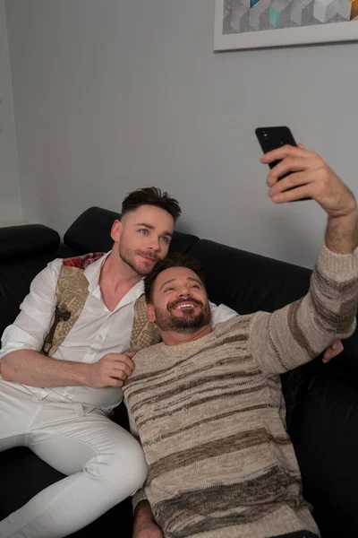 Concepto de relación homosexual. Pareja gay romántica relajándose en el sofá. novios tomando selfie con smartphone —  Fotos de Stock