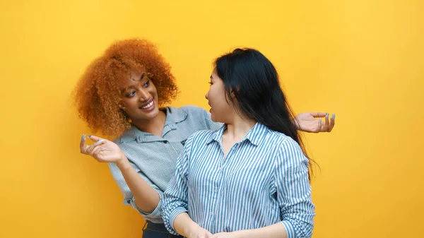 Wielorasowa koncepcja przyjaźni. Młode afrykańskie czarne i azjatyckie kobiety stojące przed żółtą ścianą — Zdjęcie stockowe