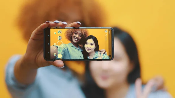Две молодые девушки, лучшие друзья используют смартфон, чтобы сфотографировать. Делать гримасы — стоковое фото