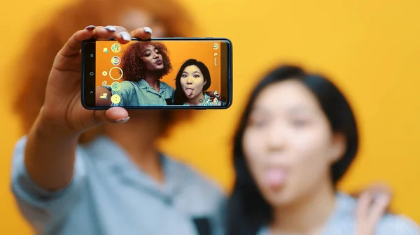 Duas meninas, casal lésbico usando smartphone para tirar fotos. Fazendo caretas — Fotografia de Stock