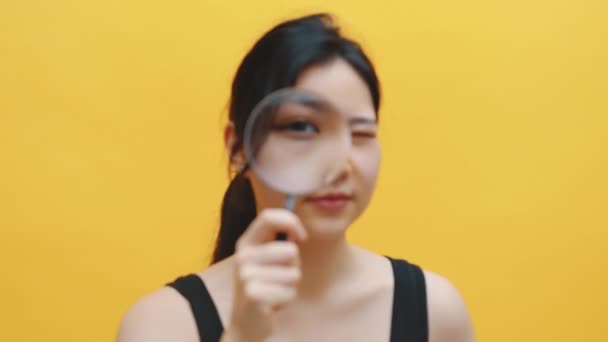 Young asian girl looks through a magnifying glass. Vision test. Female spy investigating — Stock Video