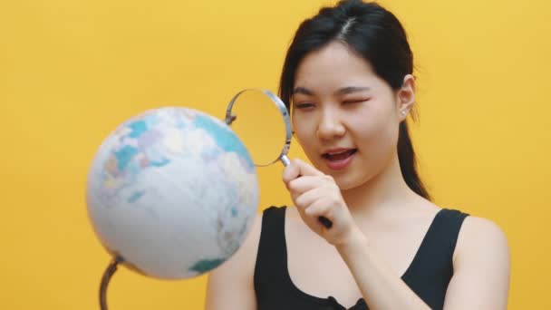 Giovane donna asiatica guardando il globo attraverso la lente di ingrandimento. — Video Stock