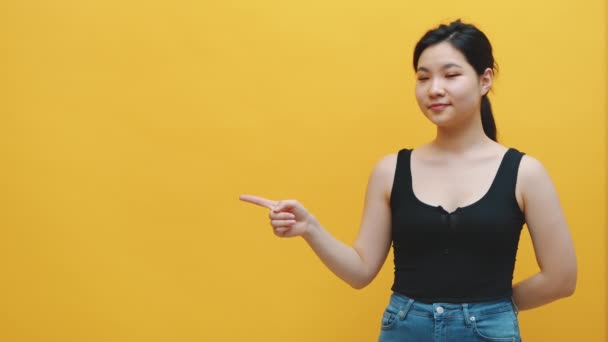 Young excited asian woman pointing finger on an empty space, yellow background — Stock Video