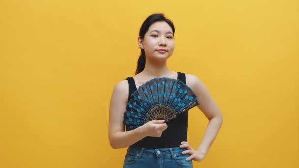 Sexig ung asiatisk kvinna poserar med blie spets fläkt över gul bakgrund — Stockvideo