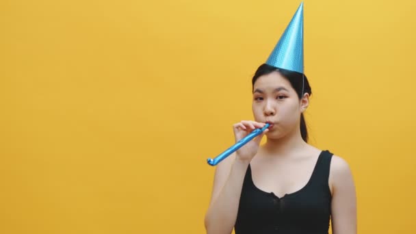 Cute asian woman with party hat blowing into the party whistle and showing thumb up. Party and celebration concept — Stock Video