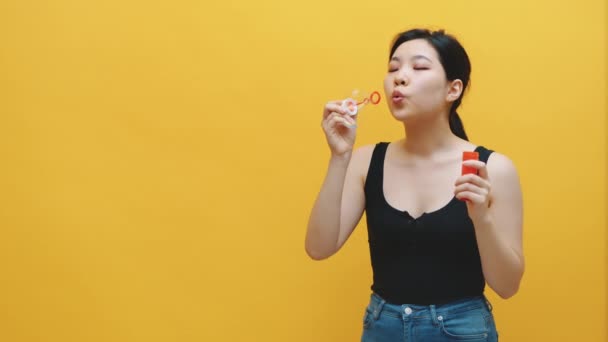 Feliz joven asiática mujer soplando burbujas de jabón. Aislado sobre fondo amarillo. Movimiento lento — Vídeo de stock