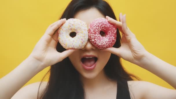 Funny young asian woman peeking through the white and pink doughnuts. Crazy funny childish woman — Stock Video