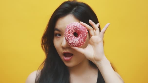 Grappige jonge Aziatische vrouw gluurt door de roze donut. Gekke grappige kinderachtige vrouw — Stockvideo