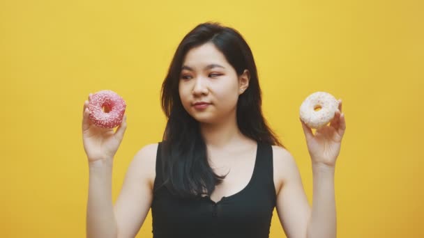 Mujer asiática joven eligiendo rosados y donas blancas en sus manos. Delicioso postre — Vídeos de Stock