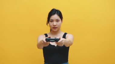 Kulaklıklı ve video oyunları oynayan eğlenceli kontrolörlü Asyalı bir kadın. Sarı arkaplanda izole edilmiş