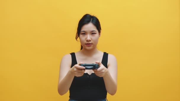 Enfocado mujer asiática joven con auriculares y controlador alegre jugando videojuegos. Aislado sobre fondo amarillo — Vídeos de Stock
