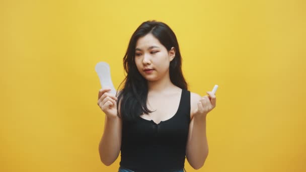 Jovem frustrado asiático mulher sofrendo de PMS. Escolha entre absorventes higiênicos e tampões — Vídeo de Stock