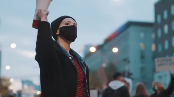 Женщина в маске для лица держит мегафон и радужный флаг. Демонстрация против дикриминации — стоковое видео