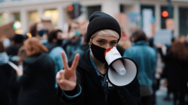 Yüz maskeli ve megafonlu bir kadın ırkçılık karşıtı protestolara destek veriyor. Barış hareketi