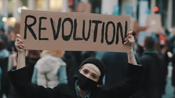 Концепция восстания. Злая молодая женщина в маске и плакате протестует в толпе — стоковое видео