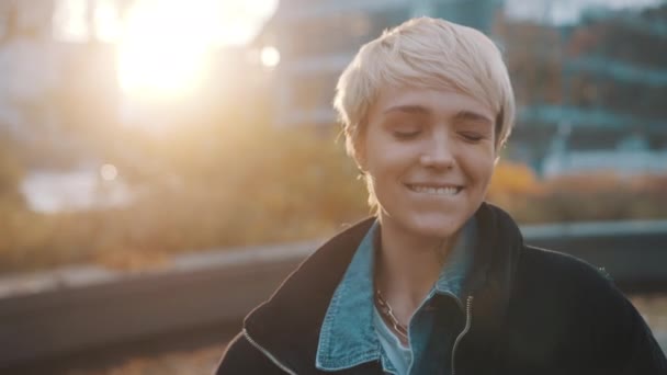Портрет молодой белокурой женщины с короткими светлыми волосами, подмигивающей в городском парке — стоковое видео