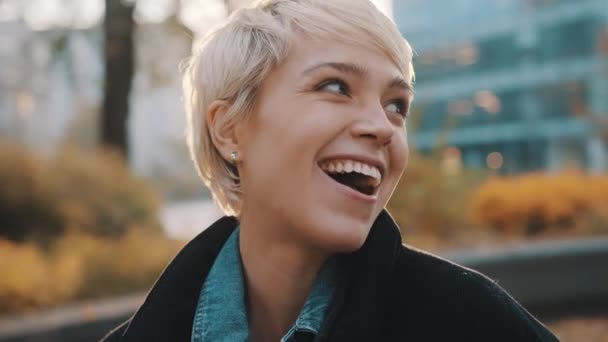 Porträt einer jungen Kaukasierin mit kurzen blonden Haaren, die im Stadtpark zwinkert — Stockvideo
