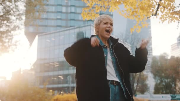 Excited young woman jumping after receiving text message in the city park in autumn — Stock Video