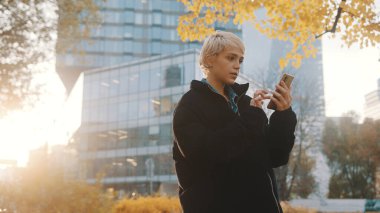 Gün batımında parkta akıllı telefon kullanan mutlu genç bir kadın.