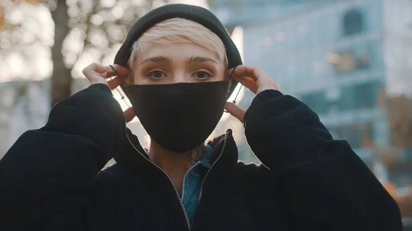 Mujer joven con chaqueta de invierno y sombrero poniéndose mascarilla. Protección contra la propagación de covid-19 — Foto de Stock