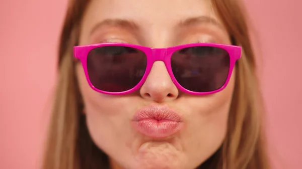 Mulher branca jovem com óculos de sol rosa soprando os lábios e enviando beijos — Fotografia de Stock