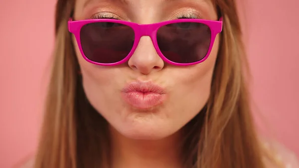 Mulher branca jovem com óculos de sol rosa soprando os lábios e enviando beijos — Fotografia de Stock