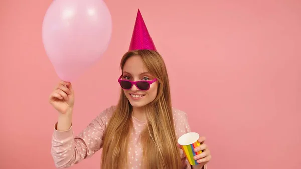 Mulher loira feliz com balão de chapéu de festa e xícara em suas mãos isolado no fundo rosa — Fotografia de Stock