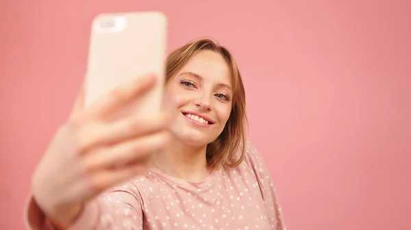 Adolescente en pijama tomando selfies usando el teléfono inteligente. Aislado sobre fondo rosa — Foto de Stock