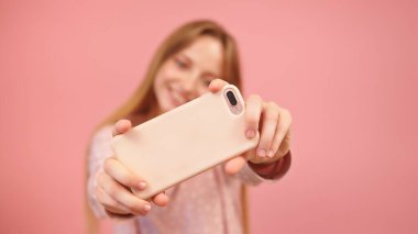 Beyaz bir kadın akıllı telefon kullanıyor ve fotoğraf çekiyor. Pembe arka planda izole edilmiş
