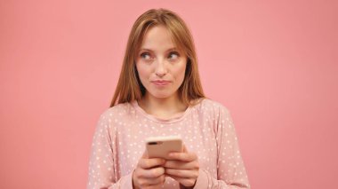 Pembe arka planda izole edilmiş akıllı telefon kullanan pijamalı beyaz bir kadın.