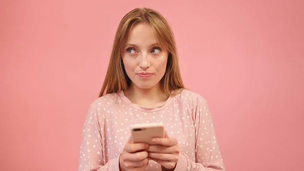 Jovem caucasiana de pijama usando smartphone, isolado em fundo rosa — Fotografia de Stock