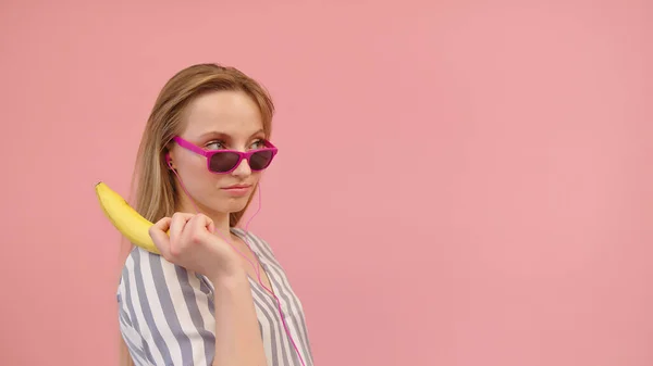 Mulher engraçada nova com óculos de sol rosa segurando banana como pistola. Espaço de cópia — Fotografia de Stock