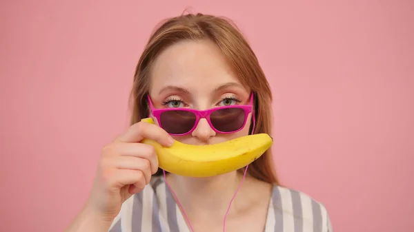 Retrato de mulher loura caucasiana engraçada segurando banana sobre os lábios. Isolado sobre fundo rosa — Fotografia de Stock