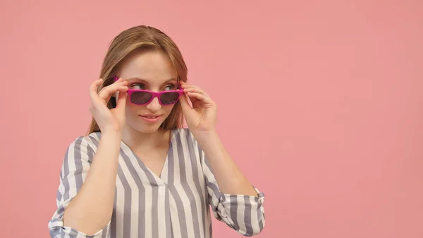 Hübsche junge kaukasische Frau im gestreiften Hemd blickt über die rosa Sonnenbrille — Stockfoto